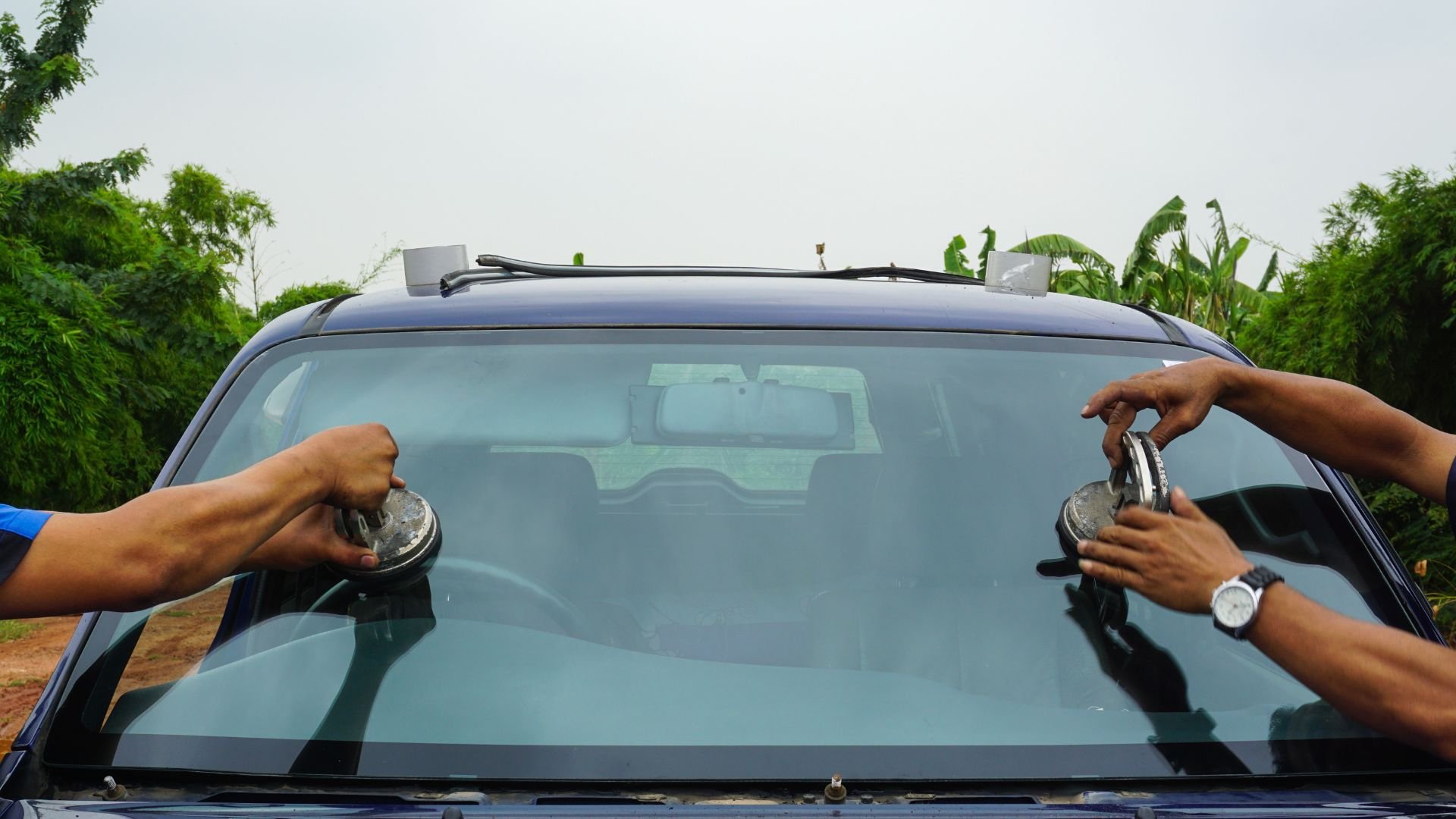 Technicians replacing windshield using suction cups on blue car