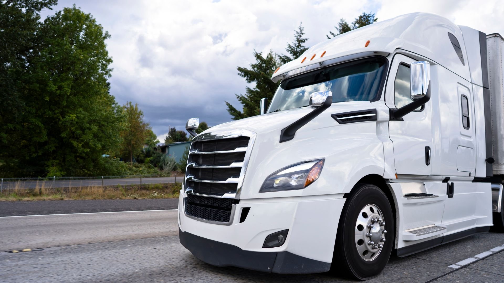 White semi-truck parked on roadside with trees and cloudy sky